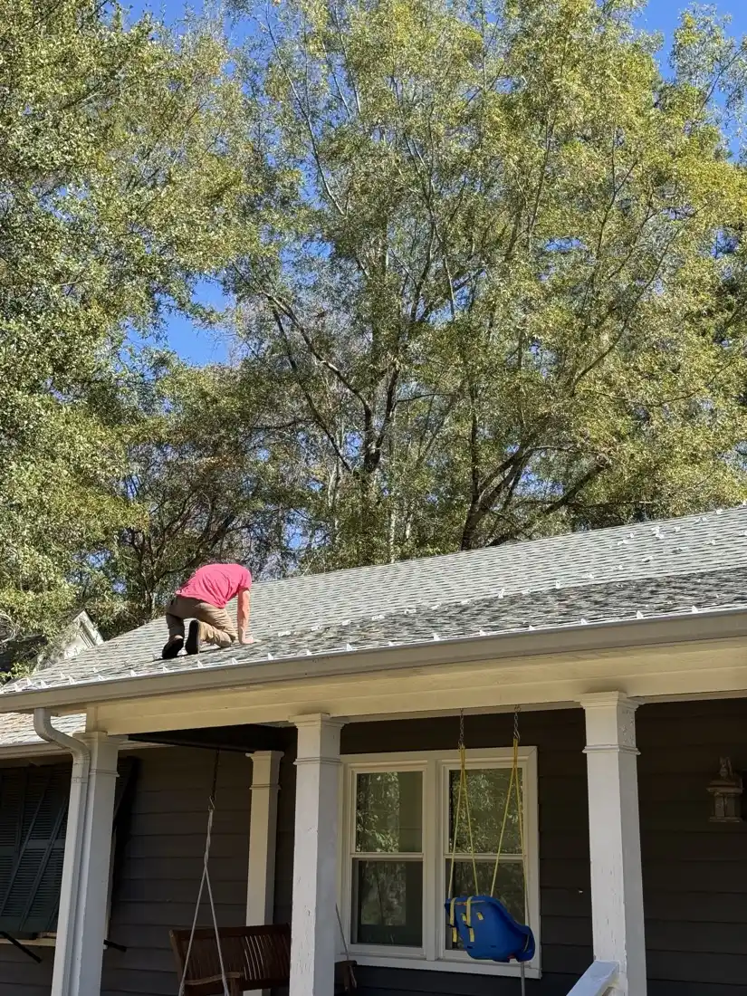 AJ Phillips kneeling on a shingle roof pressing light clips under the shingle edge along the gutter line, with the run already set behind him