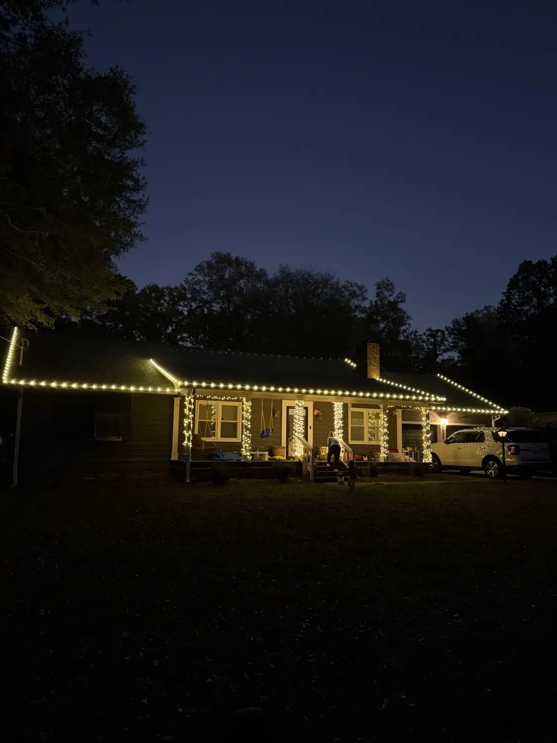 Single-storey home at dusk with warm white bulbs along the entire roofline and porch columns wrapped in mini lights from base to beam